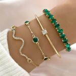 Conjunto de 4 pulseiras de cobra douradas com strass verde da Concept Áurea sobre fundo neutro.