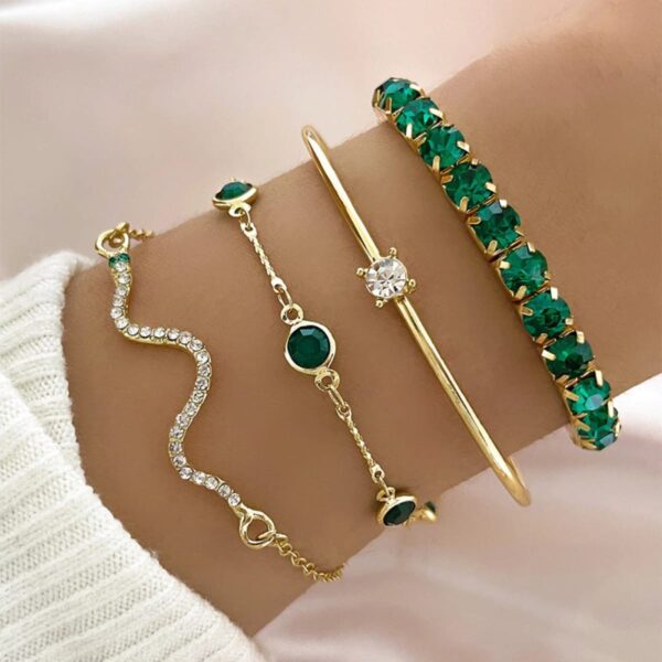 Conjunto de 4 pulseiras de cobra douradas com strass verde da Concept Áurea sobre fundo neutro.