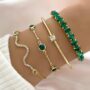 Conjunto de 4 pulseiras de cobra douradas com strass verde da Concept Áurea sobre fundo neutro.