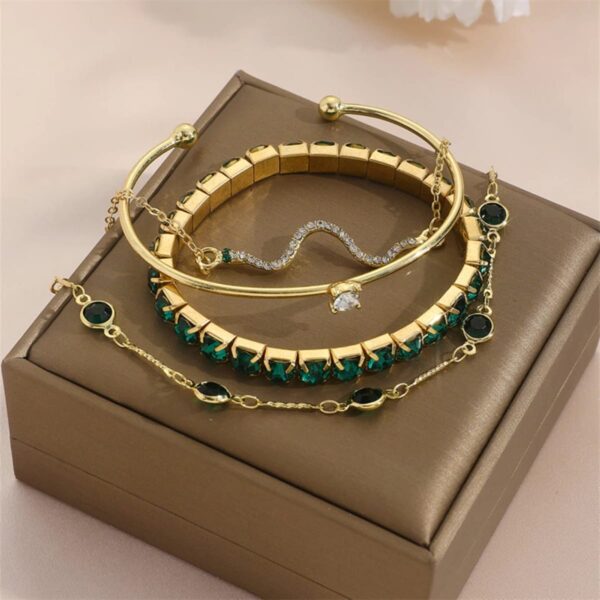 Pulseiras douradas Concept Áurea com pedras verdes e detalhes em strass sobre tecido sofisticado.